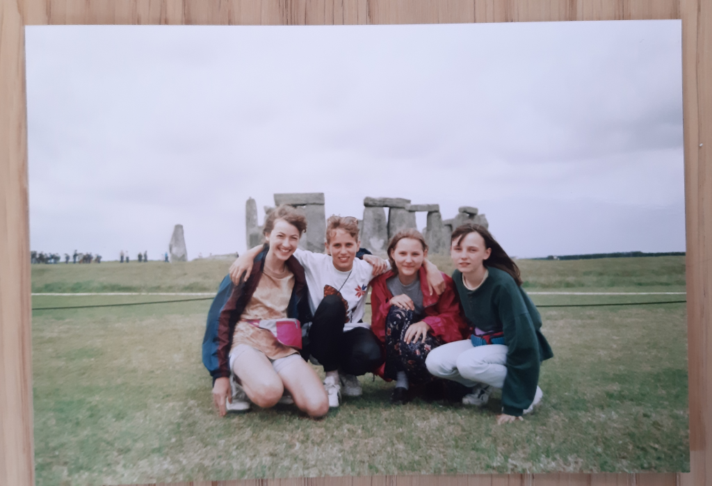 Fotka čtyř kamarádek držících se za ramena před Stonehenge.